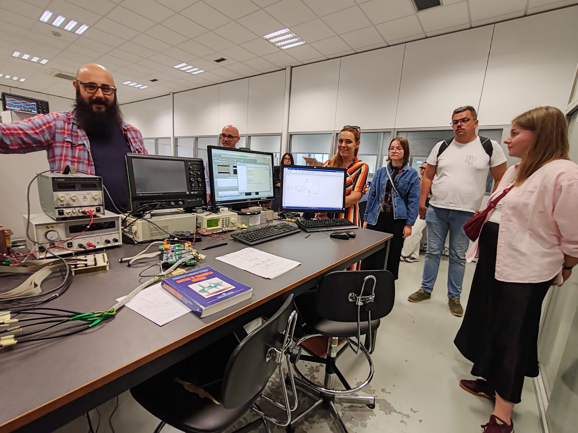 zdjęcie przedstawiające pracowników IE w jednym z laboratoriów wraz z osobą oprowadzającą, widoczne na zdjęciu jest stanowisko komputerowe systemów kontroli