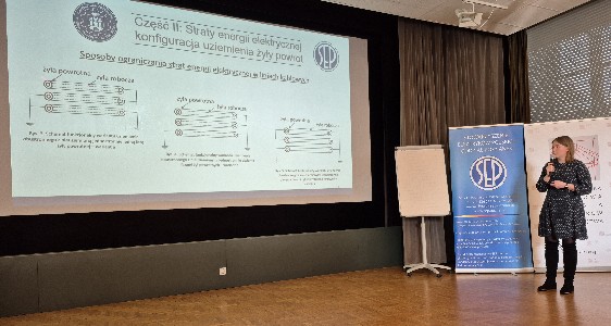 zdjęcie przedstawiające dr inz. A. Schött- Szymczak podczas prezentacji. Prelegentka stoi po prawej stronie, po lewej widoczny jest ekran z wyświetloną prezentacją