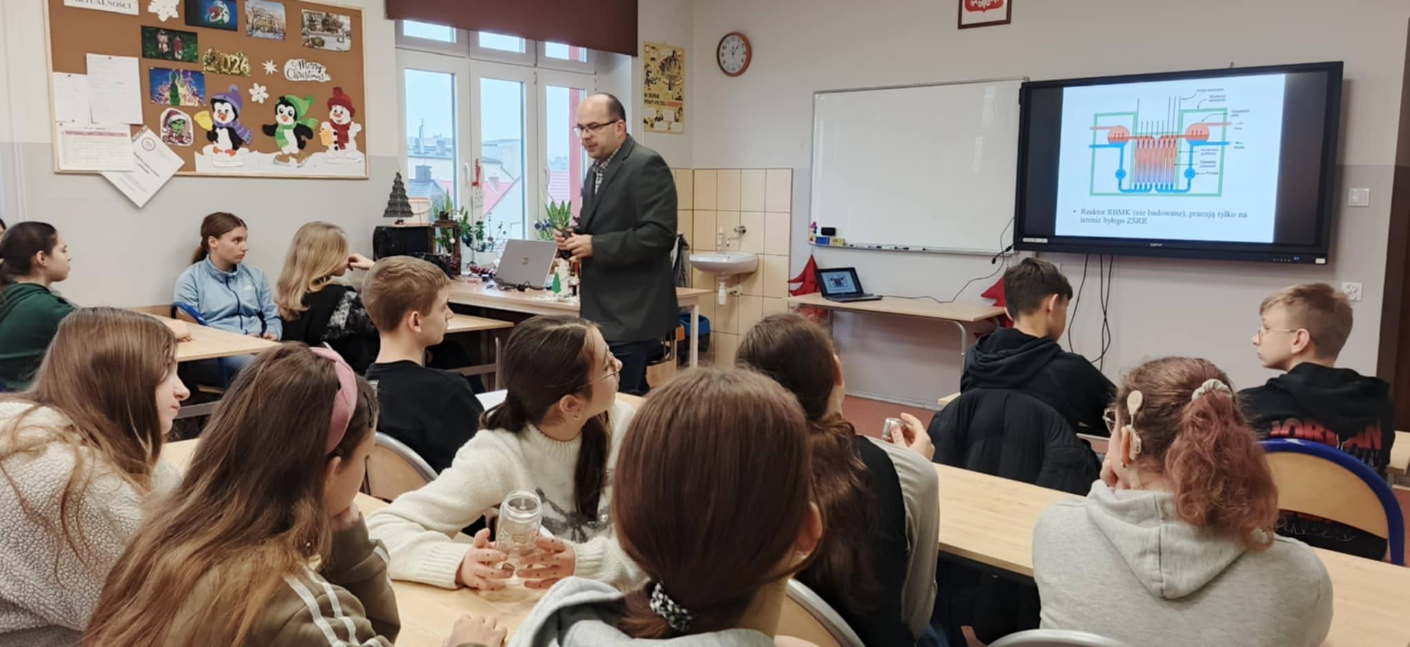 zdjęcie przedstawiające uczniów siedzących w ławkach , na środku klasy stoi prof. B. Ceran