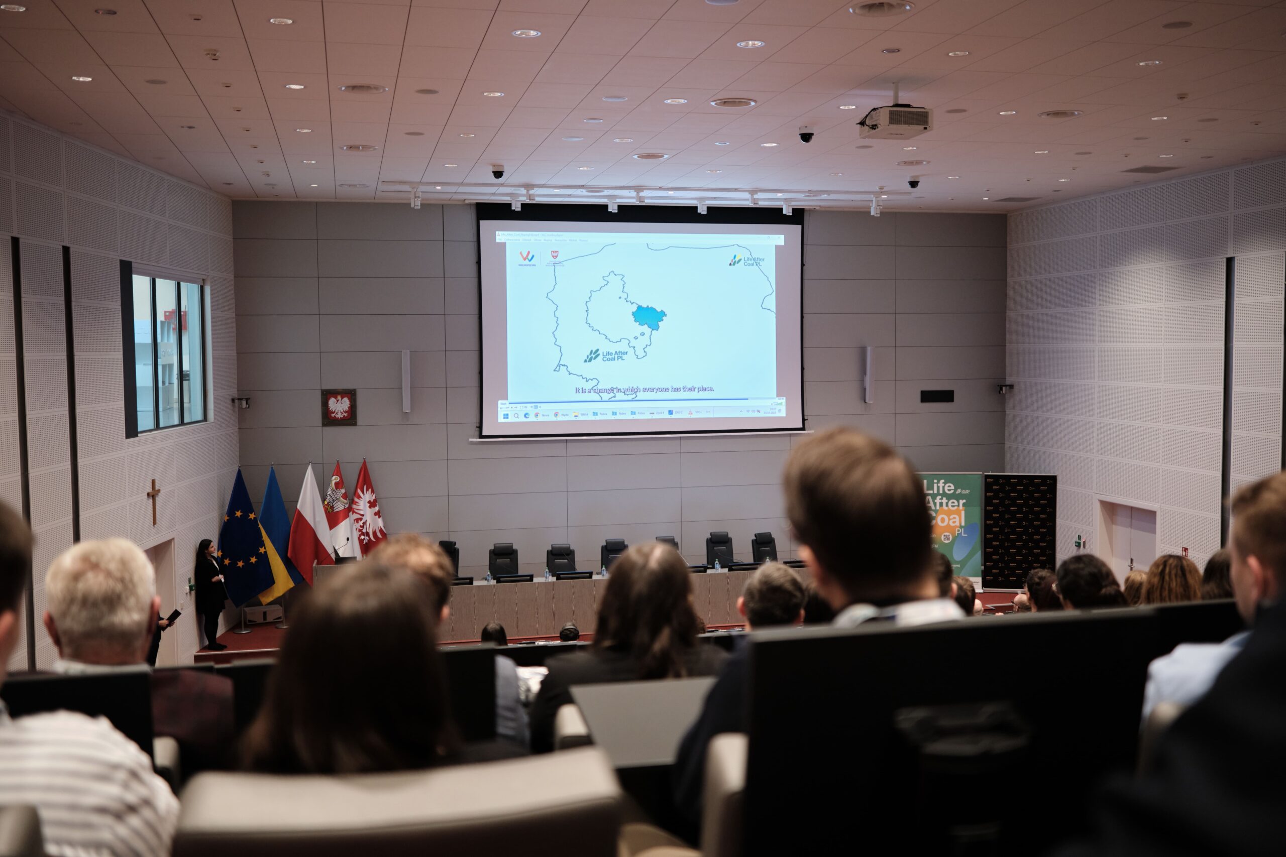 Zdjęcie przedstawiające salę wykładowo-konferencyjną, widok z foteli na rzutnik i katedrę