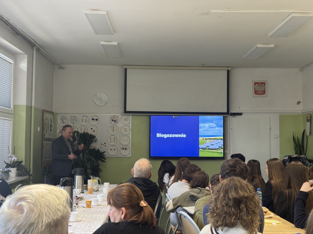 zdjęcie przedstawiające salę, w której odbywa się wykład dr inż. R.Szczerbowskiego (przedstwiony na zdjęciu po lewej stronie), z przodu widoczni uczestnicy konkursu, opiekunowie oraz zaproszeni goście